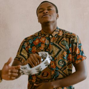 African American man wearing floral shirt enjoying music with a tambourine indoors.