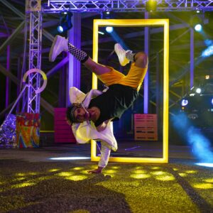 Energetic breakdance with vibrant neon lights and colorful artwork backdrop.